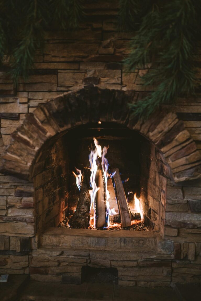 A rustic stone fireplace with logs burning brightly, creating a warm and cozy atmosphere.