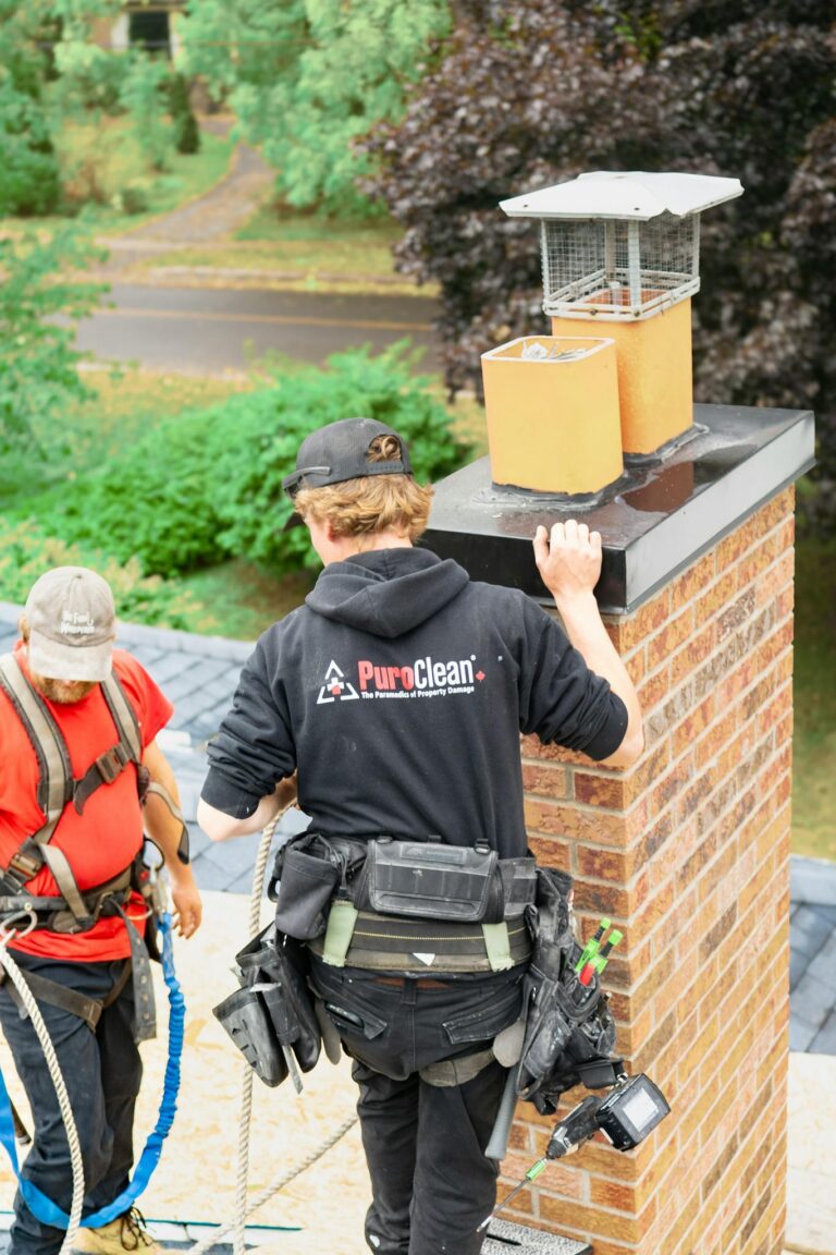 Two workers conducting a thorough chimney inspection on a rooftop in a wooded neighborhood.